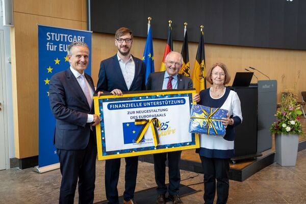 Geschenkgeber präsentieren einen symbolischen Scheck und ein Geschenkpäckchen in Gelb und Blau