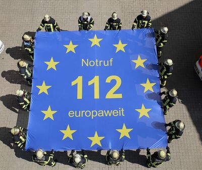Feuerwehrmannschaft spannt eine Plane mit der europaweiten Notrufnummer 112 auf